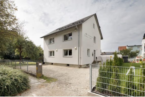 Modernes zweistöckiges Haus mit Garten und Terrasse, umgeben von Bäumen.